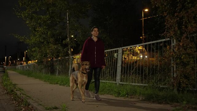 Young woman is walking her dog on a night street