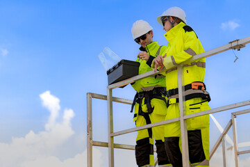 A team of engineers in high visibility safety gear stand together at a wind farm, conducting inspections and discussing renewable energy projects. Wind turbines surround them under a clear sky.