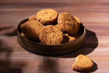 Oatmeal cookies in a plate on a brown wooden table for breakfast. Hard light.