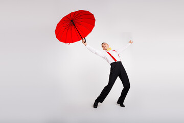 Young man dancing energetically with a red umbrella against a white background in vintage style...