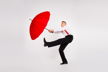 Energetic young man dancing with a red umbrella on a white background with elegance and humor
