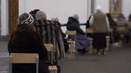 Adult nuns and temple attendants sit on chairs near pipe with holy water. Believers came to church for consecrated sanctified water during Feast of Baptism of Jesus in winter. Strange religious ritual