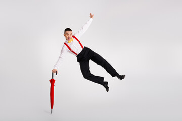 Young man leaps joyfully with vibrant red umbrella against white background, embodying dance and...