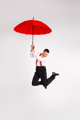 Energetic young man jumping with red umbrella against white background, showcasing elegance and...