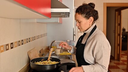 Woman cooking vegetable paella in a kitchen, wearing an apron and focused