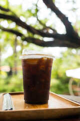 Iced americano in transparent plastic glass on the table in the garden nature background and bokeh light