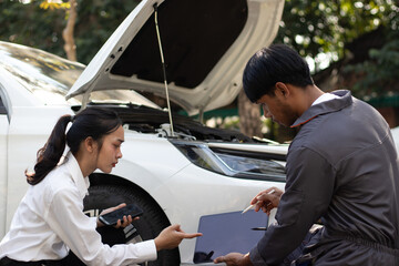 A young man and a car insurance company representative are inspecting the damage to the front of a...
