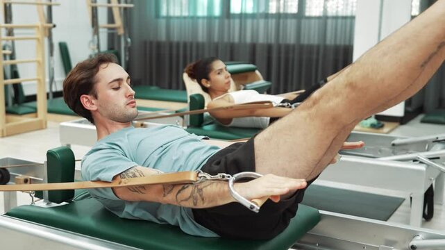Group of client perform a leg raise on a reformer machine. Pilates partner doing teaser pose on the reformer and strap for improving balance and enhancing coordination during the exercise. Habituate.