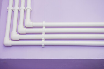 Plastic pipes are fixed to wall. Pipeline is bent. Pipes with angle of 90 degrees. Lilac wall with...