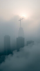 Obraz premium Urban architectural skyscrapers in dense morning fog, misty cityscape