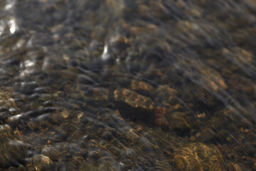 Rippling water over smooth riverbed stones with natural light reflections