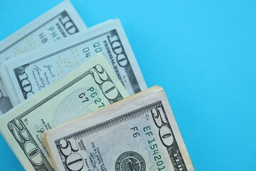 Big amount of hundred, fifty and twenty dollar bills in thick stack lies on bright blue color paper...