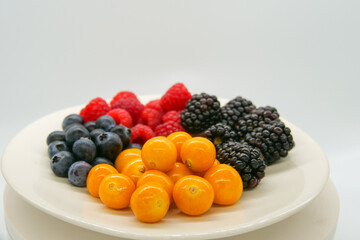Brightly colored fresh berries on a white plate in front of a white background