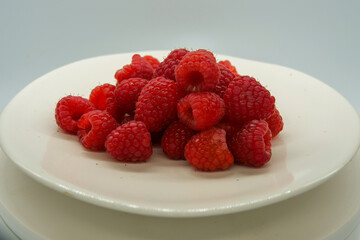 Fresh red raspberries on a white plate in front of a white background