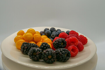 Brightly colored fresh berries on a white plate in front of a white background