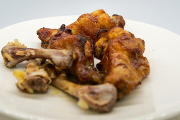 White plate with small brown basted and cooked chickenwings  and some chicken bones of wings that...