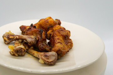 White plate with small brown basted and cooked chickenwings  and some chicken bones of wings that has been eaten.