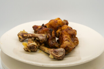 White plate with small brown basted and cooked chickenwings  and some chicken bones of wings that has been eaten.