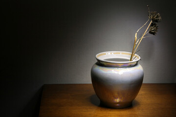 White mother of pearl vase standing on wooden surface against primed canvas background