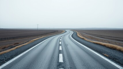 Fototapeta premium Empty asphalt highway curving through a flat, desolate landscape under a hazy sky