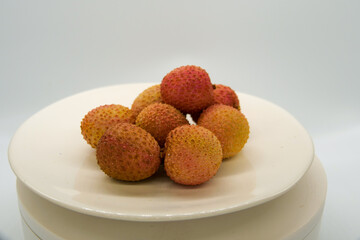 Fresh litchi fruit on a white plate in front of a white background