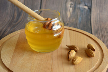 a jar of honey with wooden stick and some nuts on the cutting board