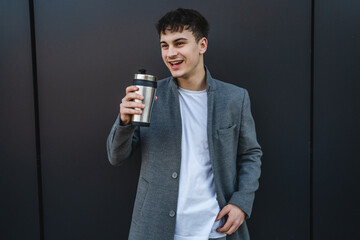 young handsome man drink coffee from thermos on the black wall background