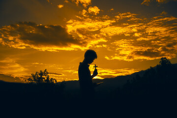 man standing praying and holding christian cross for worshipping God at sunset background. christian silhouette concept.