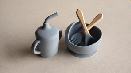 Silicone baby tableware set in gray, the first soft cup for toddlers. Baby eating utensils. Nutrition and feeding concept