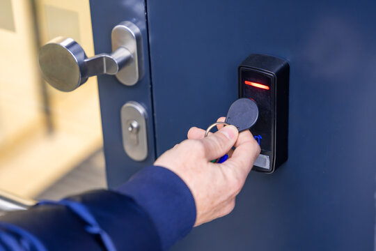 Close up view of person using a electric lock key fob to access a building via a reader of entry system mounted on a house wall