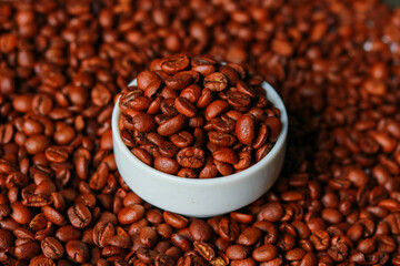 Coffee beans in white cup on roasted coffee beans background.