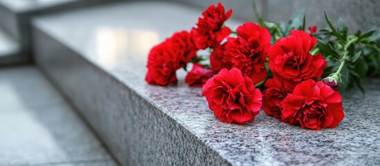 Red carnations resting on granite stone near a commemorative monument symbolizing remembrance and tribute to loved ones lost.