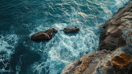 Obraz premium Breathtaking aerial view of rocky coastline with waves crashing against breakwater and serene blue sea