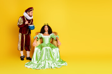 Elegant couple in vintage royal costumes posing on colorful background with yellow light