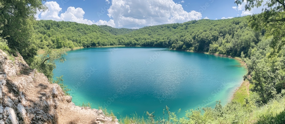 Poster panoramic view of a tranquil blue lake surrounded by lush greenery and mountains under a partly clou