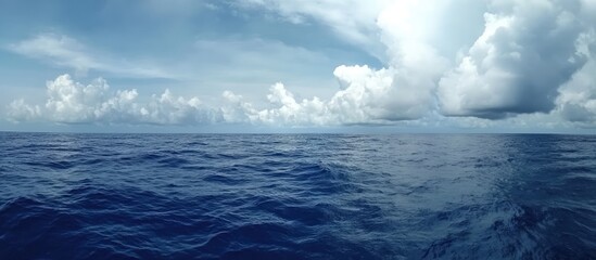 Expansive view of open ocean under a dramatic overcast sky with vibrant blue waters and fluffy white clouds in the distance