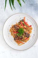 Top view of udon noodles stir-fried with tender beef, red and green bell peppers, zucchini slices, and sesame seeds.