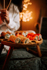 Woman Enjoys Sushi Rolls on a Festive Night With a Beautifully Decorated Christmas Tree in the Background, Embracing a Unique Holiday Culinary Experience