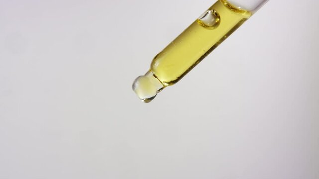 Closeup slow-motion footage of yellow oil falling from a dropper against white background