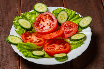 Salad, cucumbers and tomatoes in circles in a white plate on a wooden table