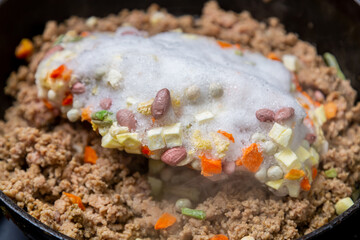 Frozen ground beef is fried in a frying pan with vegetable oil and frozen vegetables