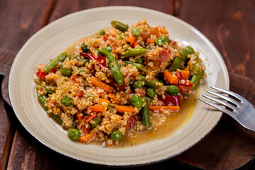 Couscous with vegetables in sauce in a plate on the table next to a fork