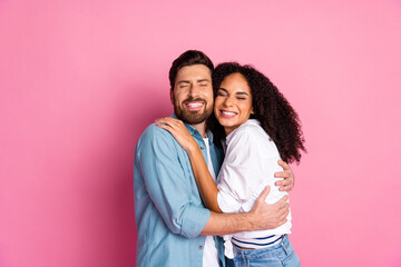 Couple smiling cheerfully while embracing against a vibrant pink background