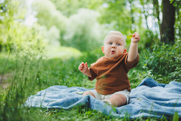 Little boy 1 year old sitting on the grass in the park and eating bread. Baby on a walk in the fresh air.