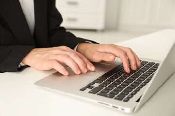 Businesswoman using laptop at white table indoors, closeup. Modern technology