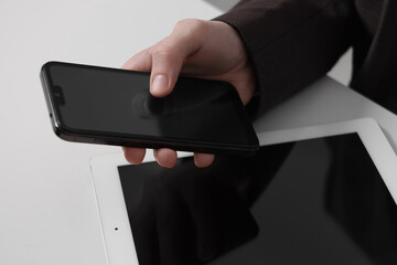 Businessman using smartphone at white table with tablet, closeup. Modern technology