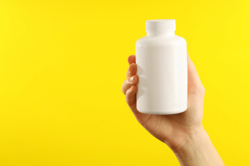 Woman holding medical bottle with pills on yellow background, closeup. Space for text