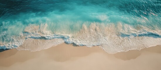 Aerial view of sandy beach meeting turquoise ocean waves under bright sunlight