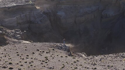Female runner navigates dusty volcanic terrain, launching dirt and rocks during high speed descent across rugged La Palma landscape, Canary Island