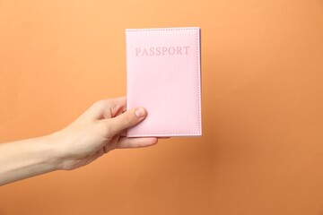 Woman holding passport in bright cover on orange background, closeup